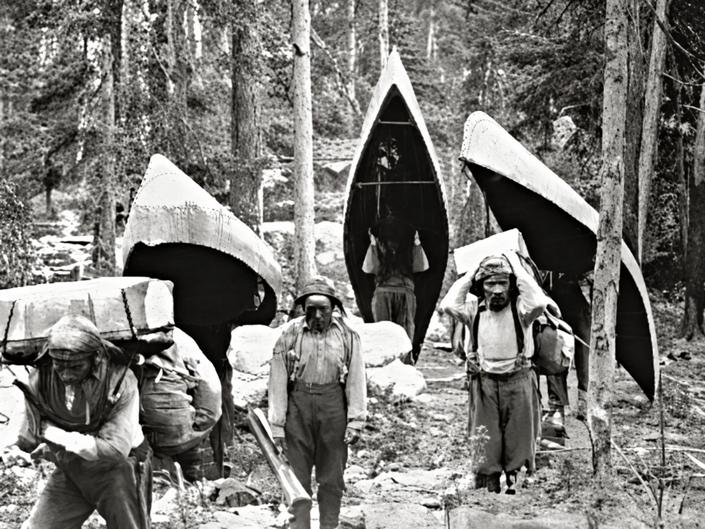 Viaggiatori indigeni che trasportano canoe nella foresta innevata
