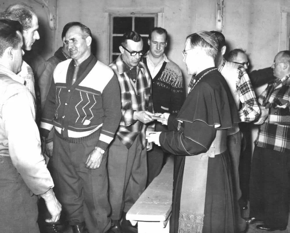 Mgr Couturier converse avec des bûcherons dans le camp